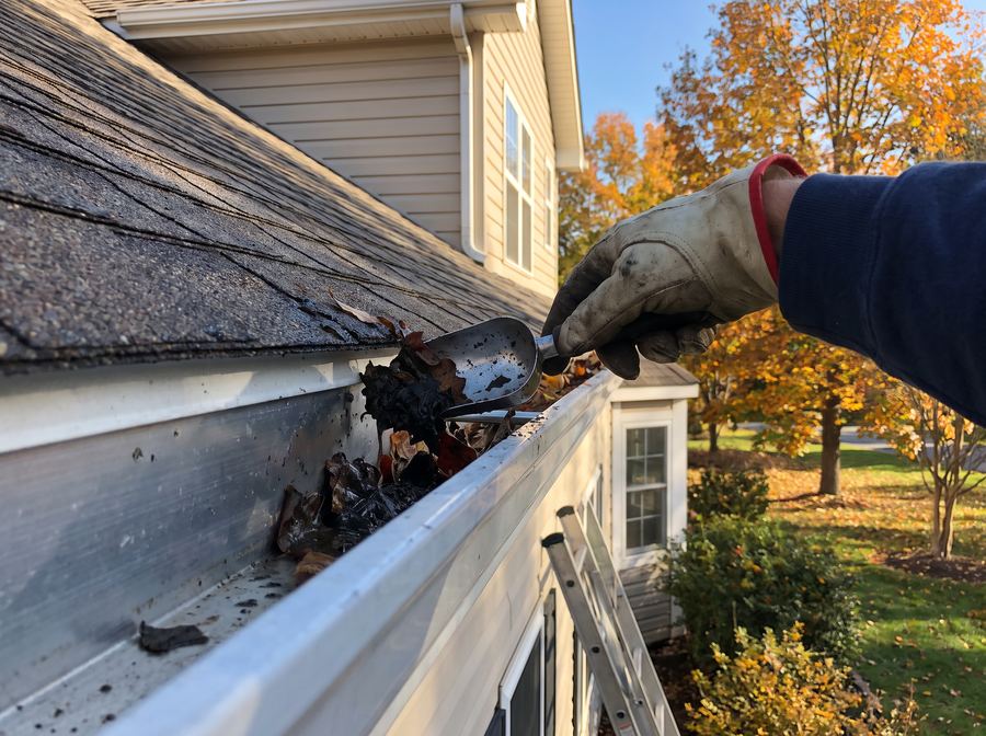 Technician clearing leaves and debris from a home rain gutter